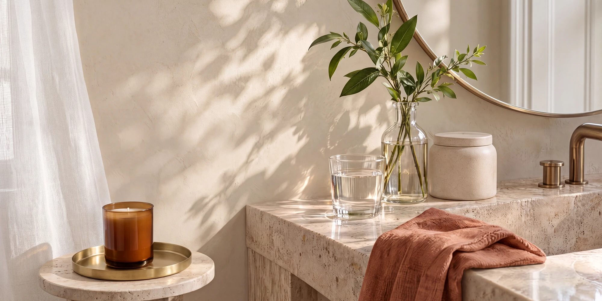 Sunlit bathroom with an amber candle, a glass vase, and water beside a stone basin