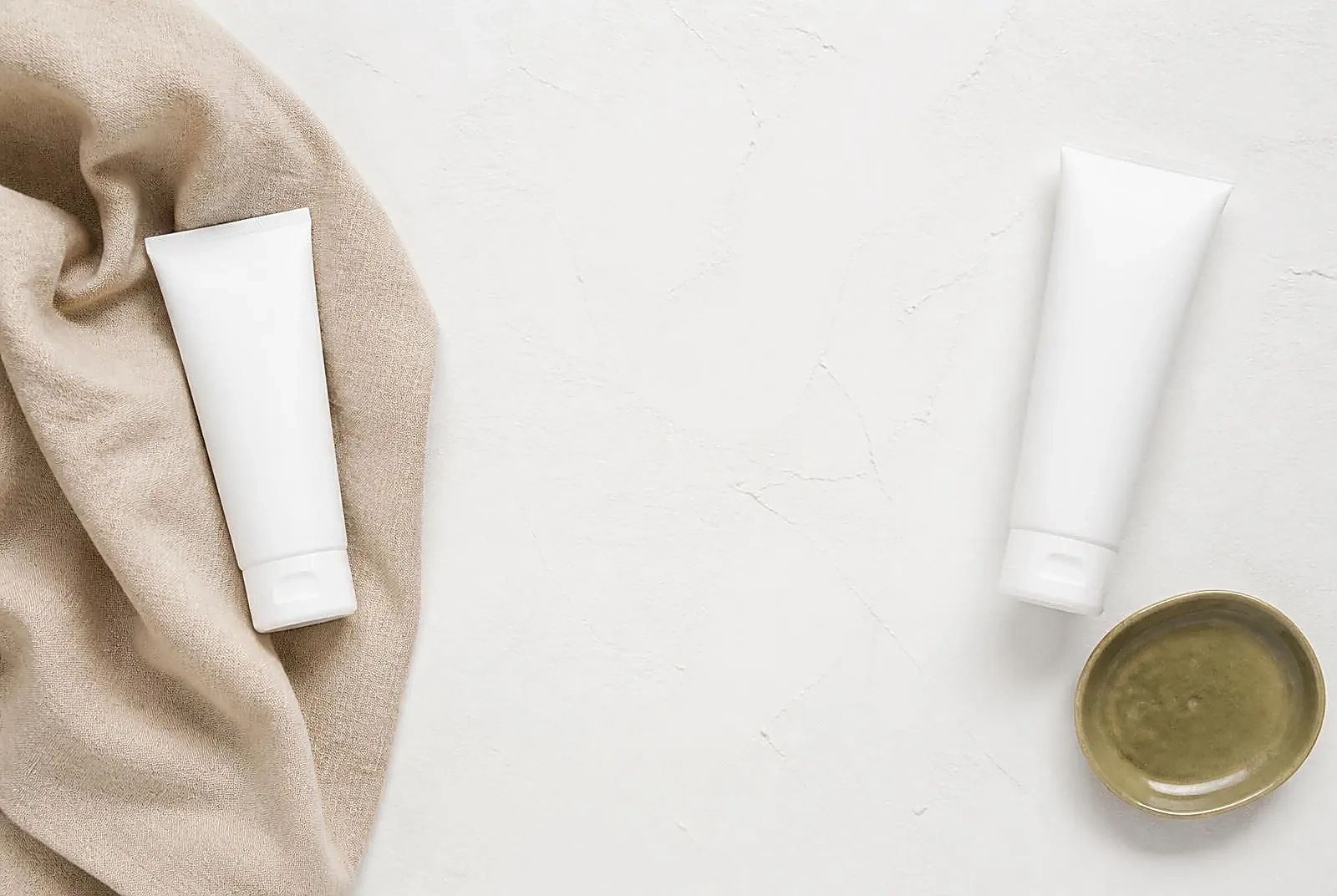 Two plain white treatment tubes placed at opposite ends of a pale plaster surface, showing actives kept apart