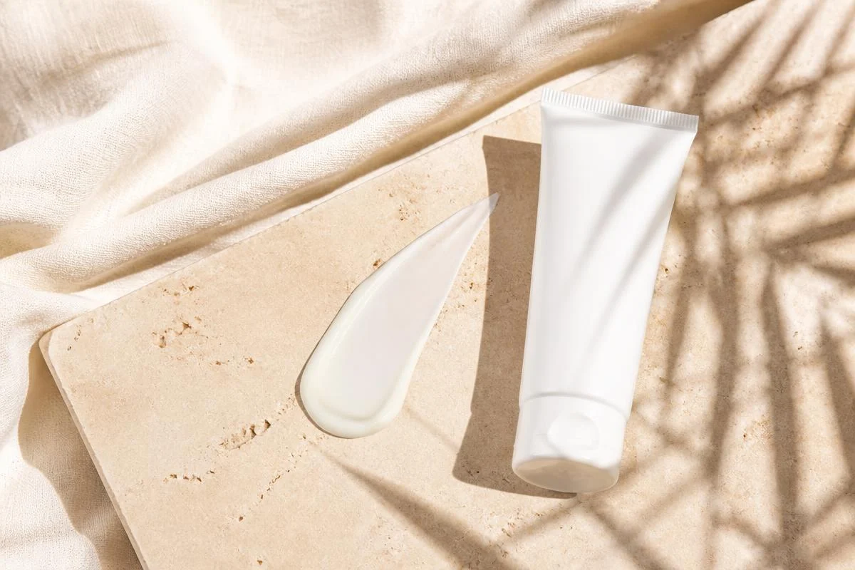 White sunscreen tube and a sheer swatch on warm sand stone in bright daylight, chosen for deeper skin tones
