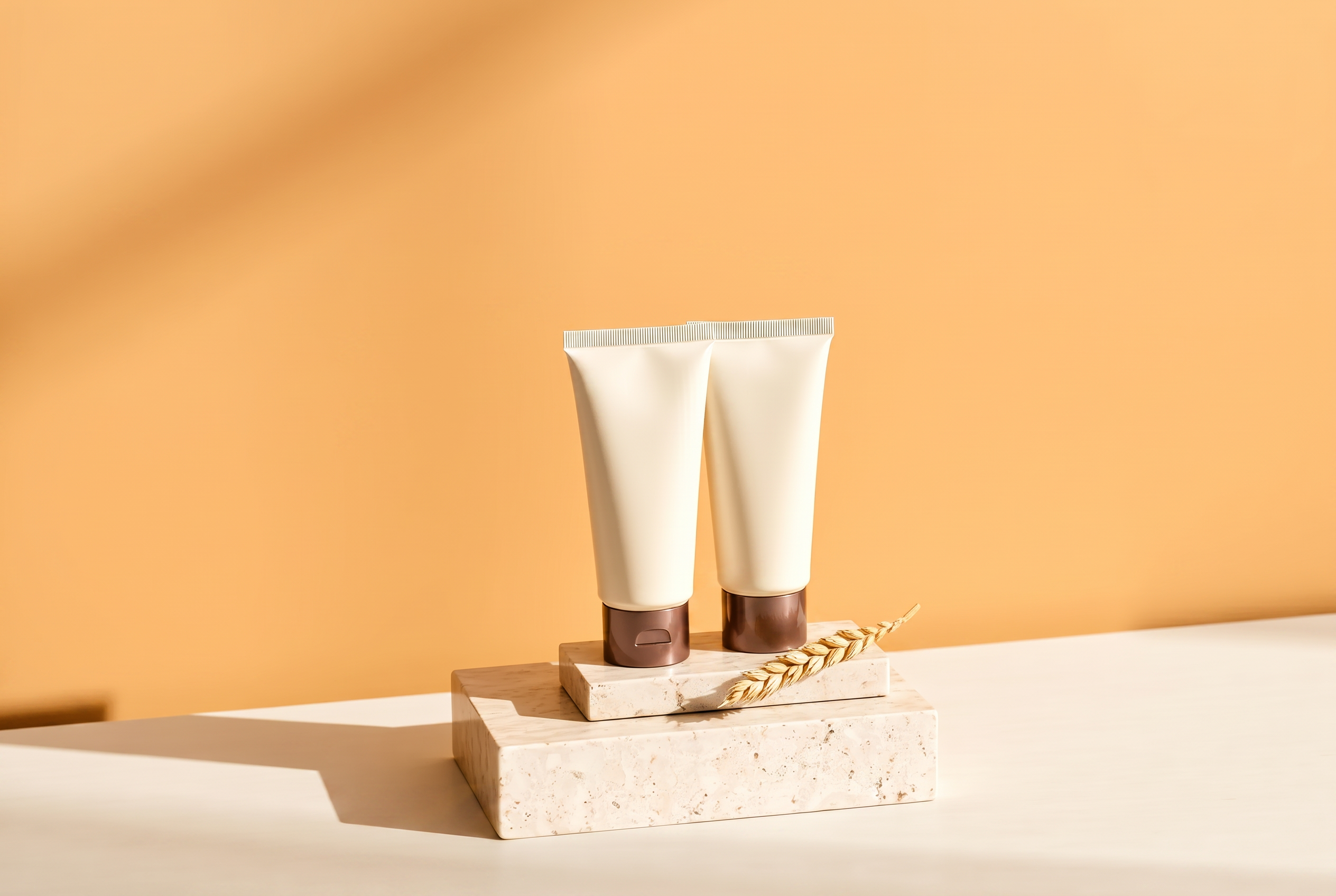 Two blank cream tubes standing on a travertine block against a warm oat wall