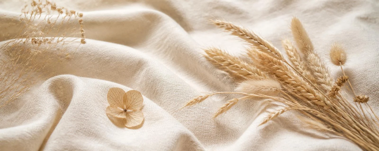 Dried wheat grasses and a pressed petal resting on folded cream linen