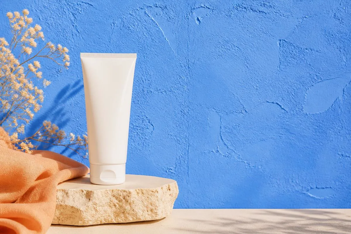 Plain white gel tube resting on a round gray marble plinth with a single clear droplet