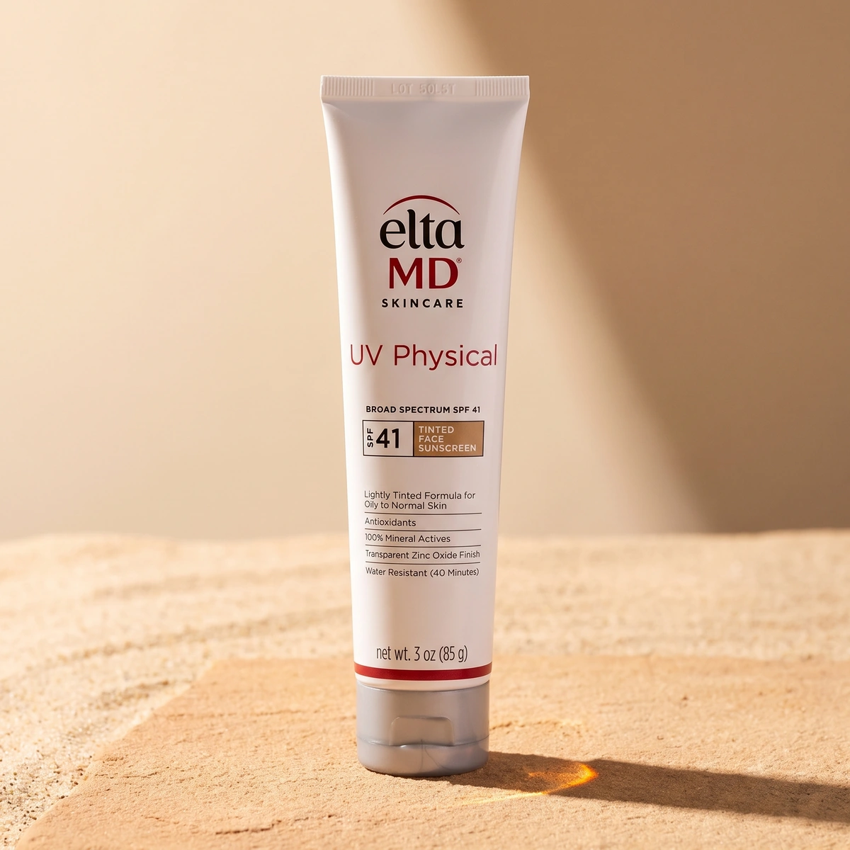 EltaMD UV Physical SPF 41 tube on warm sandstone, with a gray cap and an amber light streak