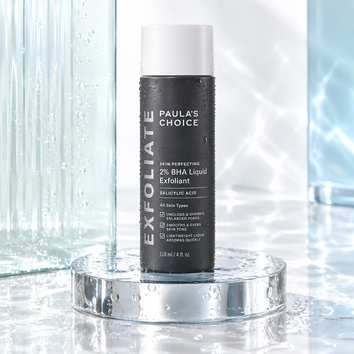 Paula's Choice 2% BHA Liquid Exfoliant bottle on a luminous wet glass and chrome stage