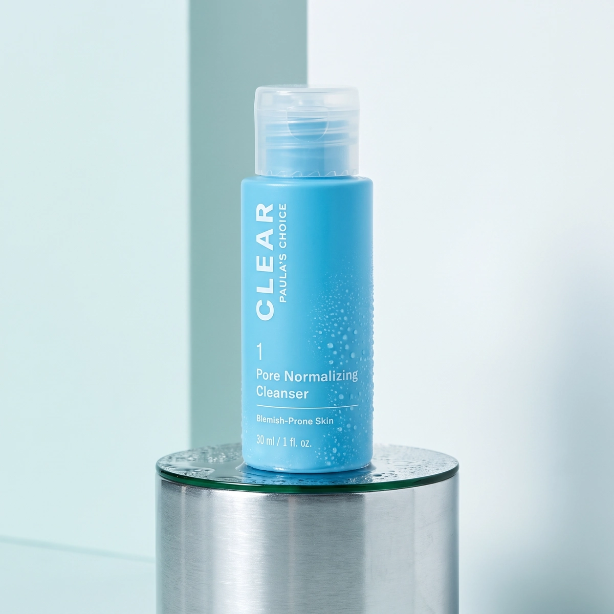 Paula's Choice CLEAR Pore Normalizing Cleanser bottle on a wet chrome pedestal, with a clear cap and clear droplets