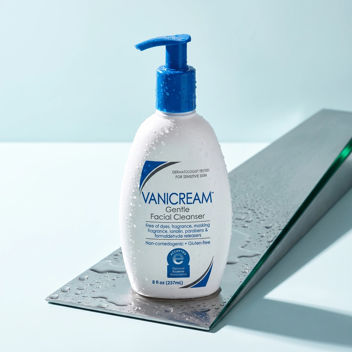 Vanicream Gentle Facial Cleanser bottle on a wet chrome plate, with a blue pump and clear droplets